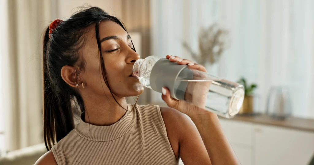 A women drinking water from a clear water bottle.