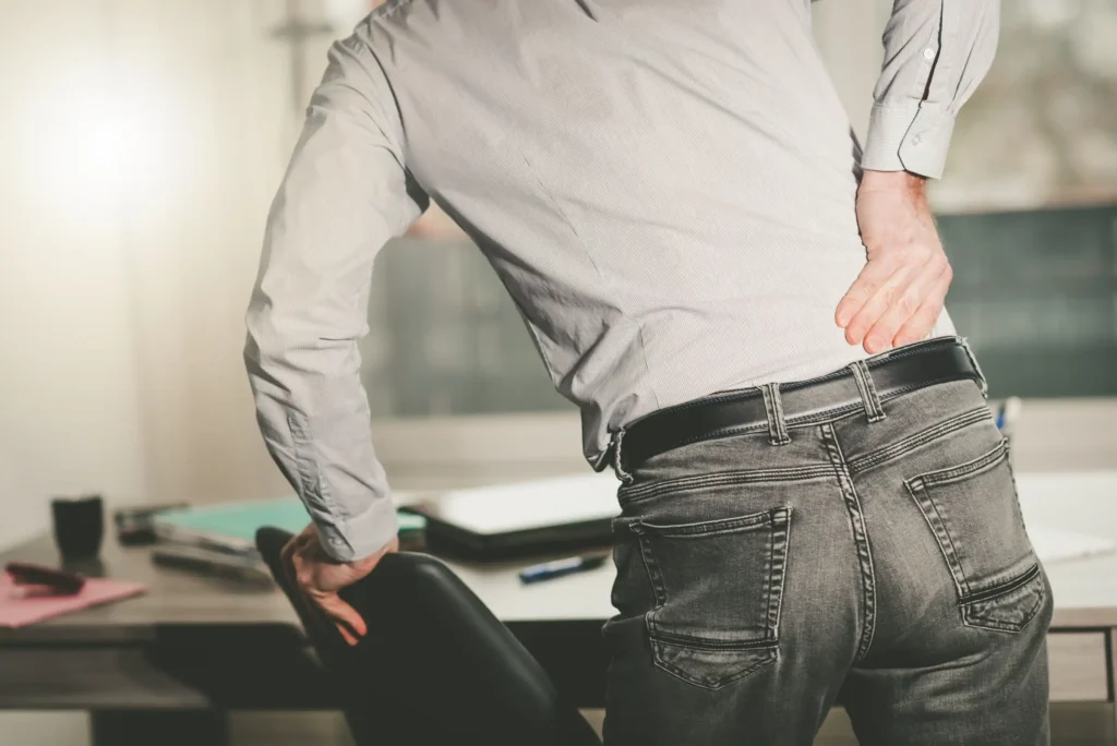 A man holding his back holding on his computer chair.