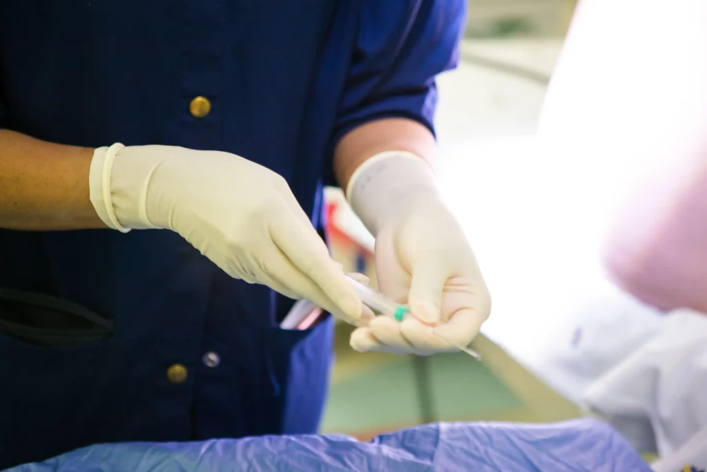 A health care professional wearing gloves with a needle under bright medical lights.