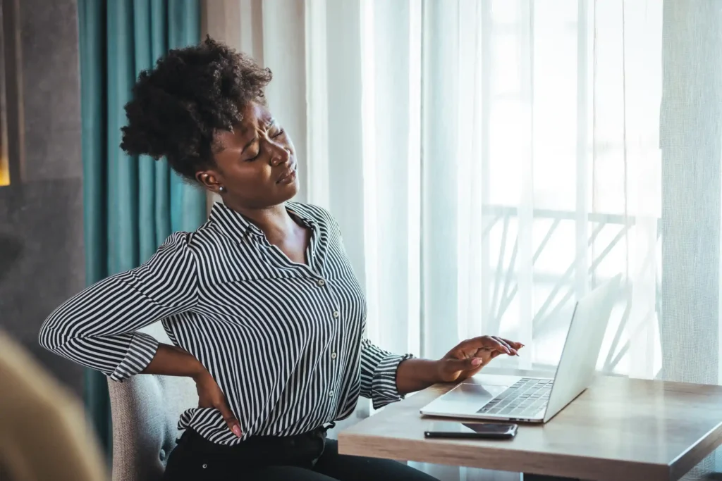 A woman working on her computer holding her back in pain.