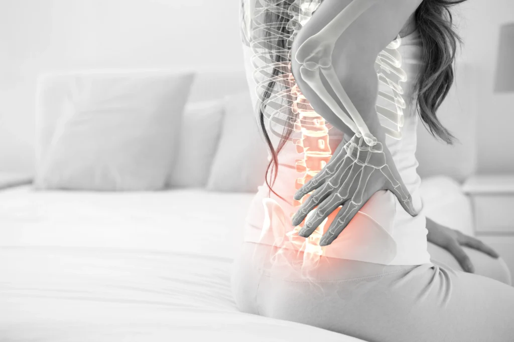 Woman holding her lower back with a digitally highlighted spine showing areas of pain or inflammation.