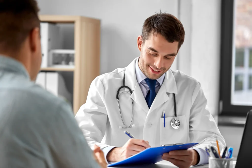Smiling doctor with a stethoscope taking notes on a clipboard while talking to a patient, representing information on what to expect during the RFA procedure.