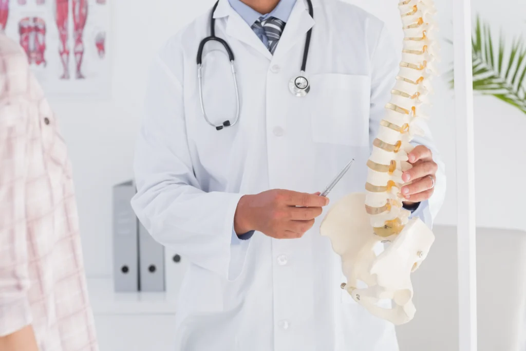 Doctor holding and pointing to a model of the human spine while discussing treatment options, representing the question of being a candidate for spinal cord stimulation.
