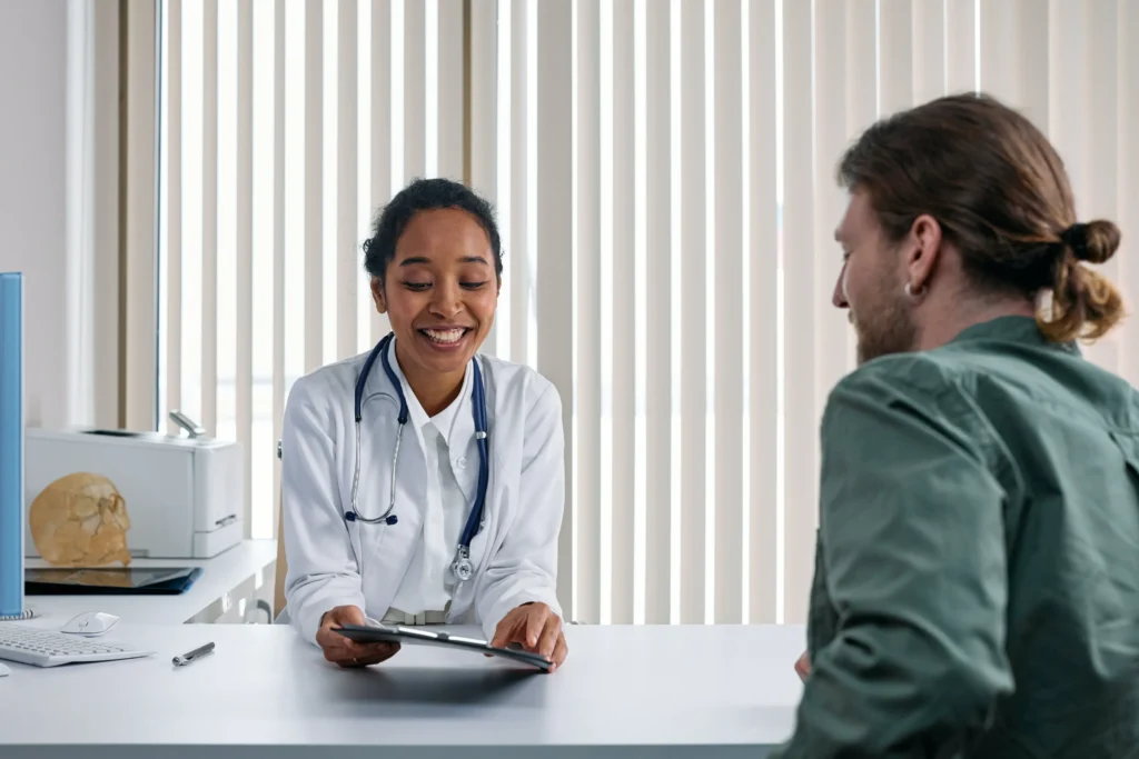 Smiling doctor with a stethoscope discussing information on a tablet with a patient, representing what to expect from the procedure.